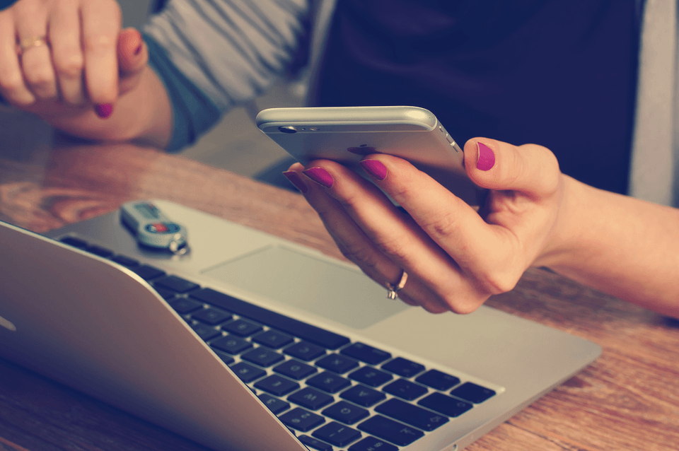 Woman holding mobile phone and working on laptop