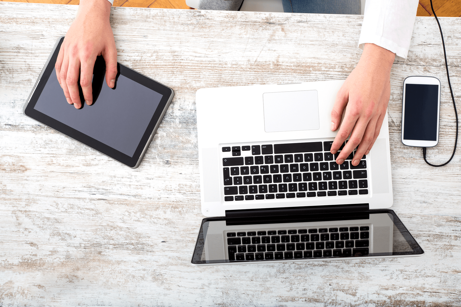 person typing on a laptop while using a tablet and mobile phone