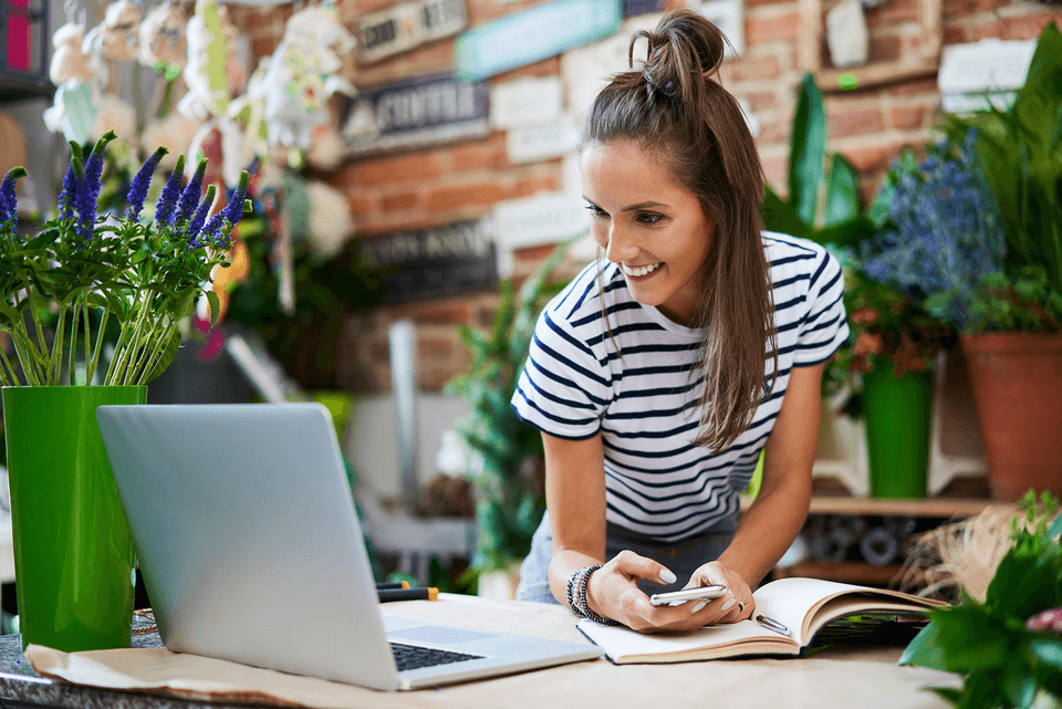 woman working on a laptop while holding a mobile phone