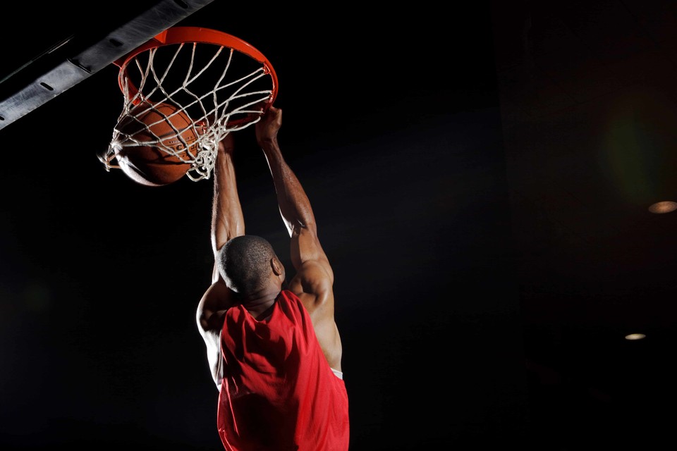 Basketball player in red jersey dunking ball through net against dark background